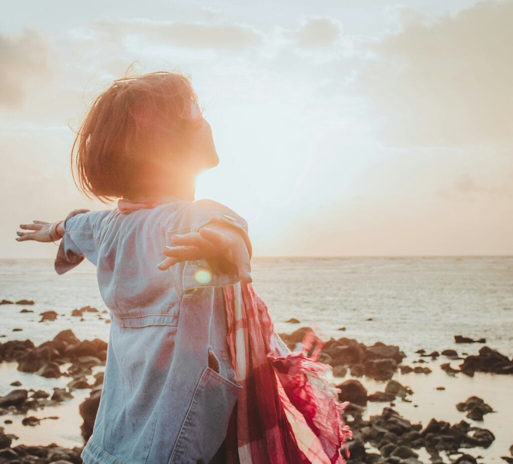 Femme bras écartée sur une plage au lever du soleil, tête haute Illustrant la liberté, la douceur, le bien-être